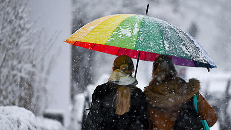 Zwei Frauen stapfen mit einem buntem Regenschirm durch den Schnee.