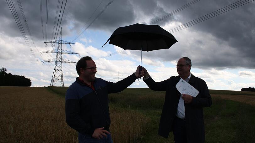 Gemeinderat Matthias Oberhofer (l.) und Bürgermeister Josef Klaus demonstrieren die elektrischen Entladungen mit einem Schirm. Was beim Berühren eines Schirms noch als Kitzelei am Finger zu spüren ist, kann laut Gutachten von TÜV-Süd für Träger von Herzschrittmachern gefährlich werden.