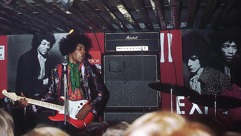 "Der Auftritt am Abend fand vor einer neu gestalteten Bühnenwand statt und Jimi hatte zu einer Grünrotschwarz gestreiften Hose ein Blumenhemd, einen bunten Seidenschal und eine indisch gemusterten Jacke an." "Der Auftritt am Abend fand vor einer neu gestalteten Bühnenwand statt und Jimi hatte zu einer Grünrotschwarz gestreiften Hose ein Blumenhemd, einen bunten Seidenschal und eine indisch gemusterten Jacke an."