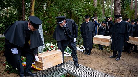 Die Gebeinekisten mit menschlichen Knochen werden nach der Trauerfeier in ein Grab auf dem Waldfriedhof Berlin-Dahlem hinabgelassen.