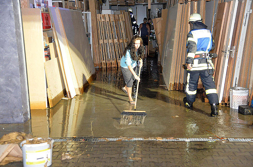 Nach einem Unwetter schiebt eine Frau in Schorndorf Wasser aus einer überfluteten Garage.