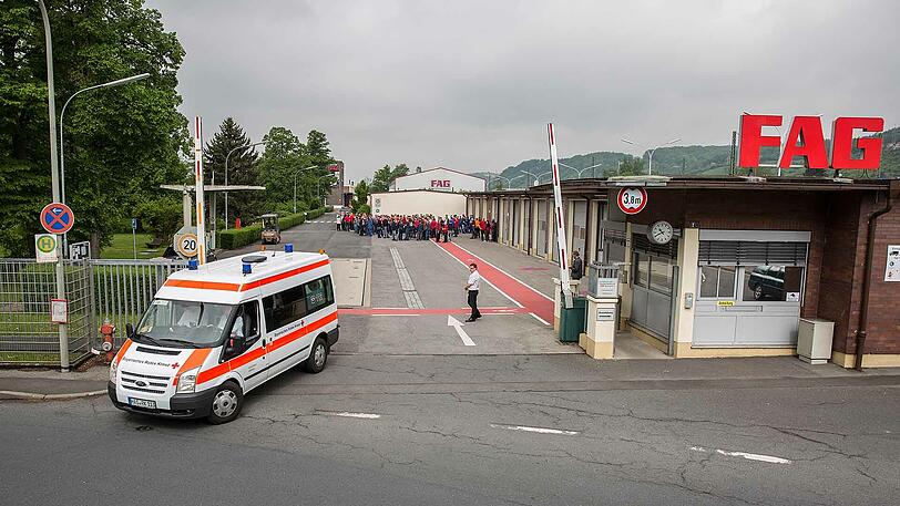 Ein Krankenwagen fährt vom Werksgelände. Im Hintergrund stehen die Mitarbeiter, die das Gebäude verlassen mussten.