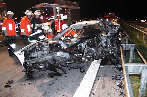 Einsatzkräfte stehen vor einem völlig zerstörten Auto.