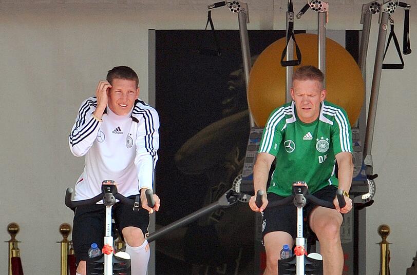 Nationalspieler Bastian Schweinsteiger (l) und Fitnesscoach Darcy Norman trainieren auf einem Ergometer am Montag