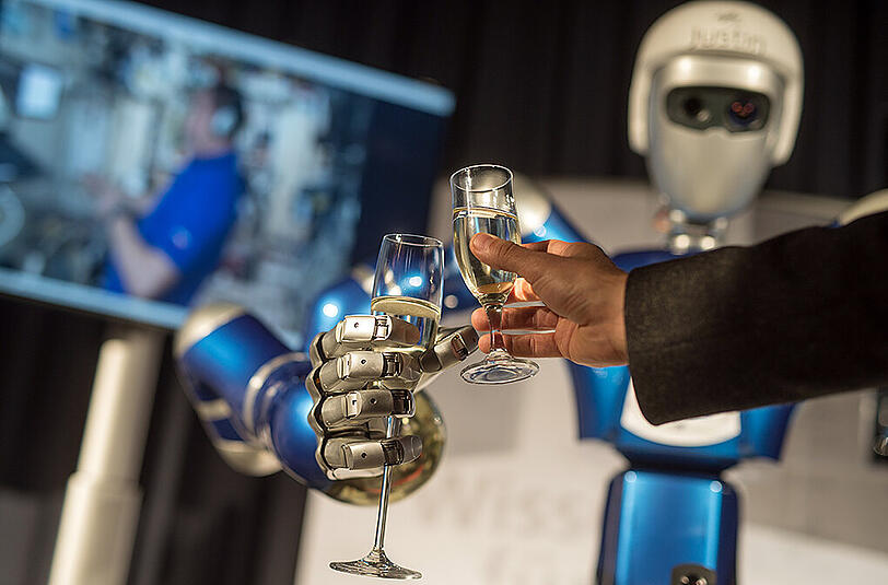 Jordi Artigas, Wissenschaftler am Institut für Robotik und Mechatronik des DLR, prostet am 17.12.2015 bei der Präsentation des Roboterprojektes "Tele-Handshake" im Forschungszentrum beim Deutschen Zentrum für Luft- und Raumfahrt (DLR) in Oberpfaffenhofen bei München dem Kosmonauten Sergei Wolkow auf der Internationalen Raumstation ISS, der den Roboter Justin steuert, virtuell zu.