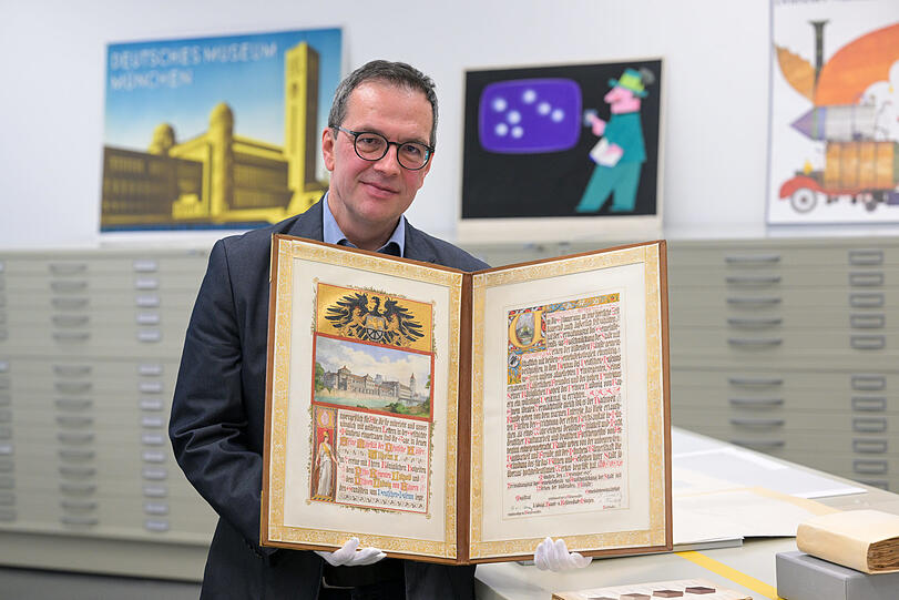 Diese Schmuckurkunde der Stadt München von 1907, die Archivleiter Matthias Röschner hier herzeigt, zeigt das Logo des Museums, Eule und Zahnrad. Den Museumsbau hat man sich damals offenbar noch anders vorgestellt, als er dann umgesetzt wurde.