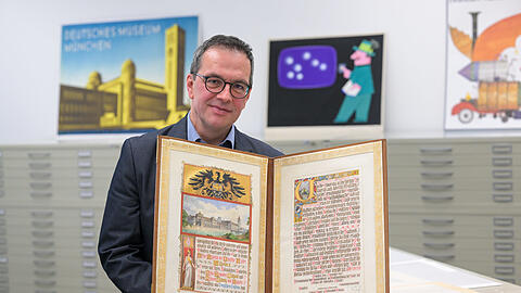 Diese Schmuckurkunde der Stadt München von 1907, die Archivleiter Matthias Röschner hier herzeigt, zeigt das Logo des Museums, Eule und Zahnrad. Den Museumsbau hat man sich damals offenbar noch anders vorgestellt, als er dann umgesetzt wurde.