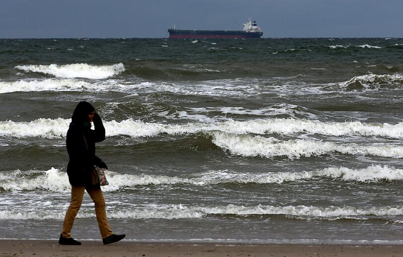 Im Ostseebad Rostock-Warnemünde (Mecklenburg-Vorpommern) ist am 30.03.2015 ein Spaziergänger am aufgewühlten Wasser unterwegs, während sich am Himmel dunkle Sturmwolken und Sonne abwechseln. Die Menschen in ganz Deutschland müssen sich auf eine stürmische Karwoche und oft auch Schnee um Ostern einstellen.