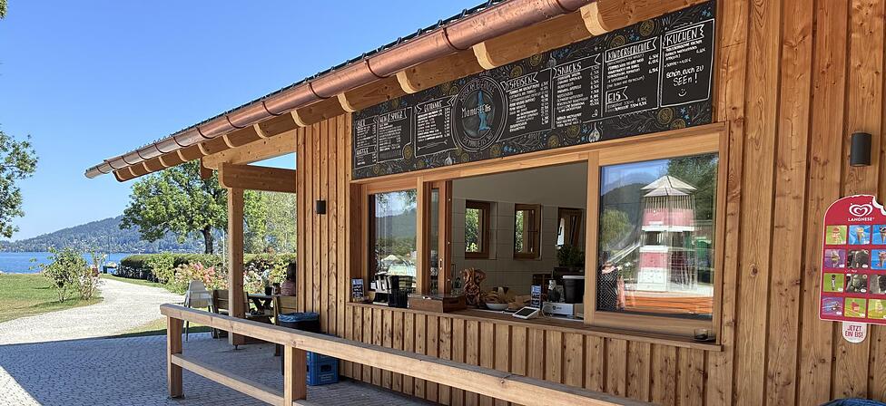Das moderne Geb&auml;ude mit viel hellem Holz in unmittelbarer N&auml;he zum Tegernsee. Der Kiosk liegt im Rottach-Egener Ortsteil Schorn &ndash; direkt neben der gro&szlig;en Badewiese &ndash; und ist bei sch&ouml;nem Wetter jeweils von 10 bis 20 Uhr ge&ouml;ffnet.