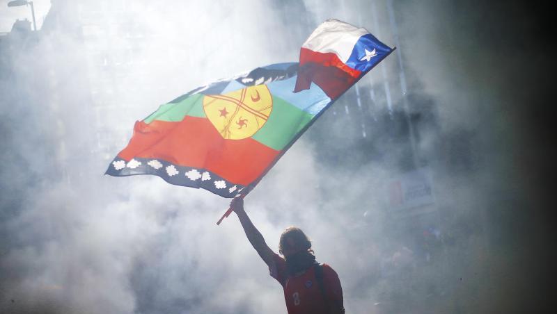 Ein vermummter Demonstrant weht die Flagge von Chile und der indigenen Gemeinschaft Mapuche mitten im Rauch während eines Protestes für Sozialreformen. Ein vermummter Demonstrant weht die Flagge von Chile und der indigenen Gemeinschaft Mapuche mitten im Rauch während eines Protestes für Sozialreformen.