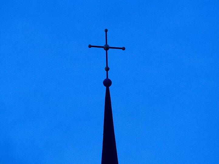 Ein Kreuz ist auf einer Kirchturmspitze zu sehen. Foto: Friso Gentsch/dpa/Symbolbild