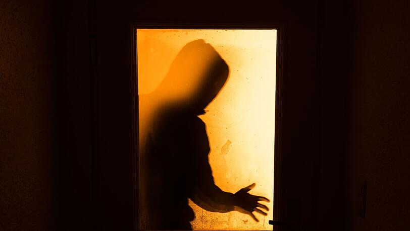 Der Schatten eines Mannes ist hinter einer gläsernen Wohnungstür zu sehen.