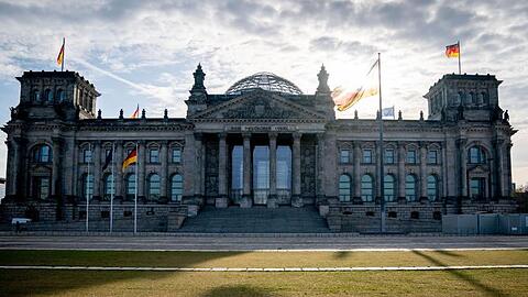 Die Sonne steht am Morgen hinter dem Reichstagsgebäude mit dem Bundestag.