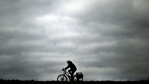 Ein Radfahrer fährt vor dem grauen Wolkenhimmel auf dem Rheindamm: In Nordrhein-Westfalen bleibt es einige Tage vor dem Jahreswechsel trotz milder Temperaturen ungemütlich.