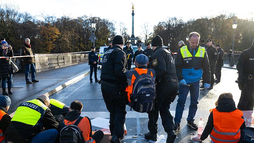 Polizisten tragen in München einen Klimaaktivisten der "Letzten Generation" weg, der sich zuvor auf der Prinzregentenstraße auf den Asphalt geklebt hatte.
