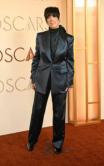 Diane Warren: Der Hosenanzug ist eine elegante und moderne Alternative zum klassischen Abendkleid und überzeugt durch seinen klaren, maskulin inspirierten Schnitt. Der glänzende Stoff sorgt für eine schöne Red-Carpet-Wirkung. Gleichzeitig wirkt das Styling im oberen Bereich etwas geschlossen. Eine Bluse oder ein Top mit mehr Kontrast oder einem geöffneten Ausschnitt hätte die Halspartie stärker betont und dem Look mehr Leichtigkeit verliehen. Diane Warren: Der Hosenanzug ist eine elegante und moderne Alternative zum klassischen Abendkleid und überzeugt durch seinen klaren, maskulin inspirierten Schnitt. Der glänzende Stoff sorgt für eine schöne Red-Carpet-Wirkung. Gleichzeitig wirkt das Styling im oberen Bereich etwas geschlossen. Eine Bluse oder ein Top mit mehr Kontrast oder einem geöffneten Ausschnitt hätte die Halspartie stärker betont und dem Look mehr Leichtigkeit verliehen.