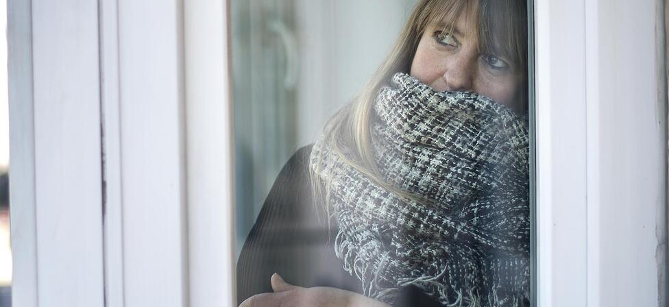 Eine Frau blickt warm angezogen aus ihrem Wohnungsfenster. In M&uuml;nchen wird es ab Donnerstag kalt.