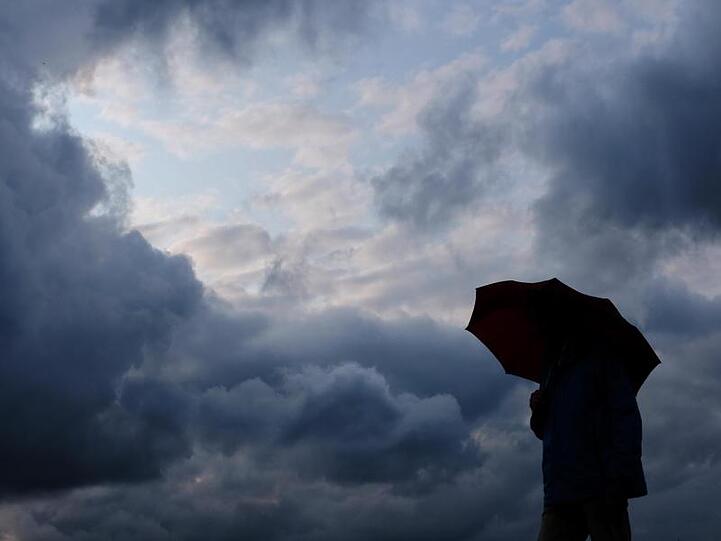 Ein Mann geht mit einem Regenschirm vor aufziehenden dunklen Wolken spazieren. Foto: Martin Gerten/Archivbild
