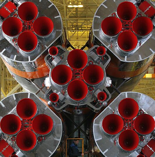 Eine Rakete vom Typ Sojus TMA-20 in einer Montagehalle im Kosmodrom Baikonur. Zwischen den beiden unteren Triebwerken ist ein Techniker zu sehen, was erahnen lässt, wie groß die Rakete ist.