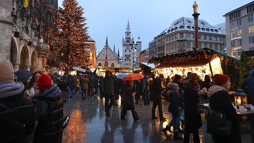 Menschen gehen über den festlich geschmückten Christkindlmarkt auf dem Marienplatz.