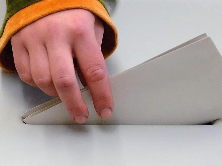 Eine jugendliche Hand steckt einen Stimmzettel in eine Wahlurne.