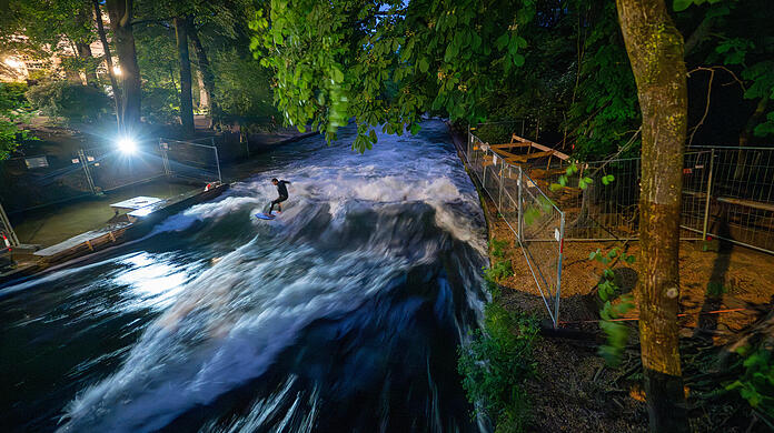 Ein Mann mit einem Surfboard reitet in den frühen Morgenstunden auf der künstliche Eisbachwelle im Englischen Garten. Nach dem Tod einer Surferin, die auf der Eisbachwelle im Englischen Garten stürzte und verstarb, soll die Welle demnächst wieder eröffnet werden.
