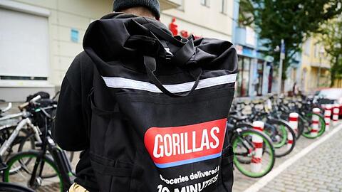Ein Beschäftigter des Lieferdienstes Gorillas trägt einen Rucksack und steht vor den Fahrrädern.