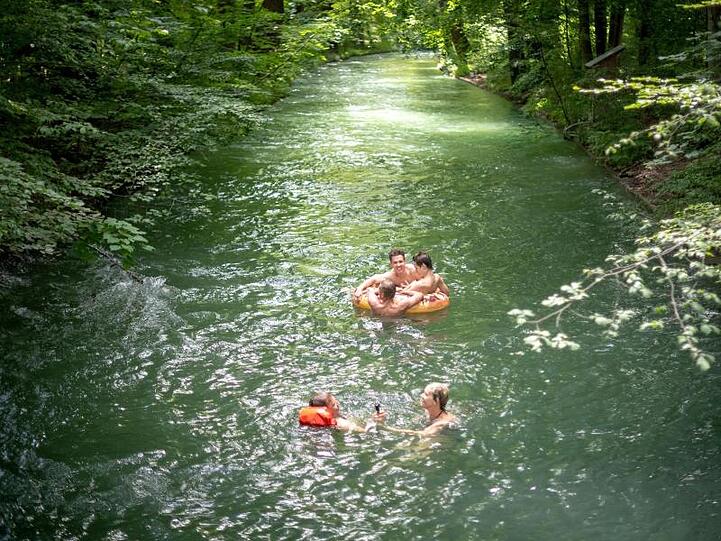 Münchner schwimmen bei warmen Temperaturen durch einen Bach im Englischen Garten. Foto: Sina Schuldt/Archiv