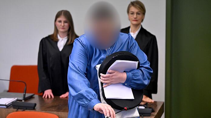 Die Angeklagte Andrea Tandler (M) steht an ihrem Platz im Gerichtssaal zwischen ihren Anwältinnen Cheyenne Blum (l) und Sabine Stetter (r).