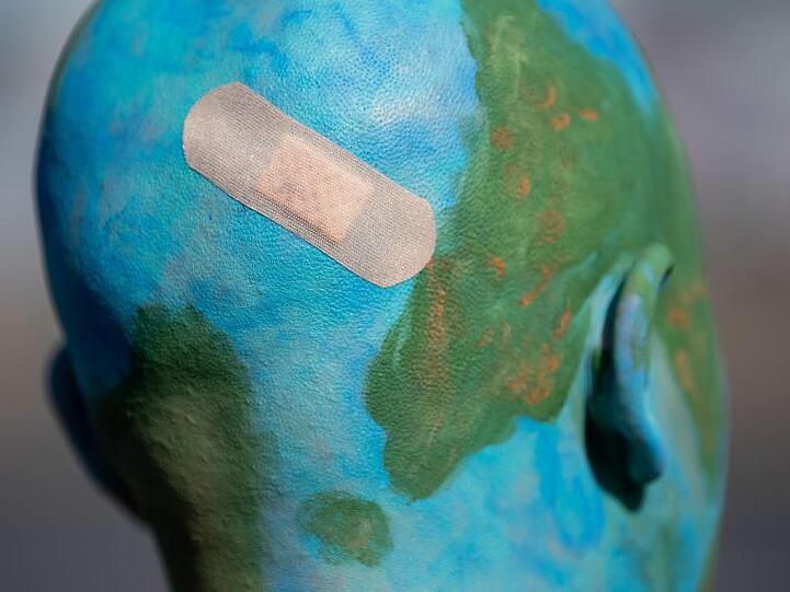 Eine Demonstrantin in Stuttgart hat sich beim Protest für mehr Klimaschutz ihren Kopf wie eine Erdkugel angemalt und ein Pflaster draufgeklebt.
