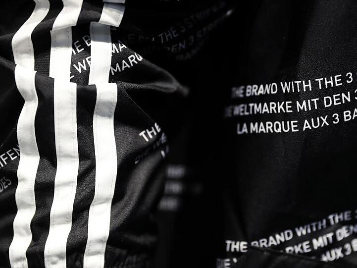 Das Logo des Sportartikelherstellers Adidas und der Schriftzug "Die Marke mit den 3 Streifen". Foto: Daniel Karmann/Archivbild