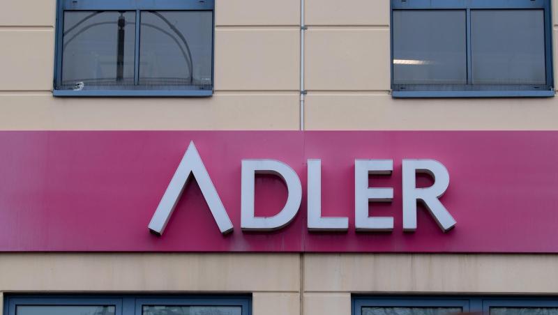 Eine Frau mit Mund-Nase-Bedeckung geht an einem Schild des Unternehmens Adler Modemärkte vorbei.