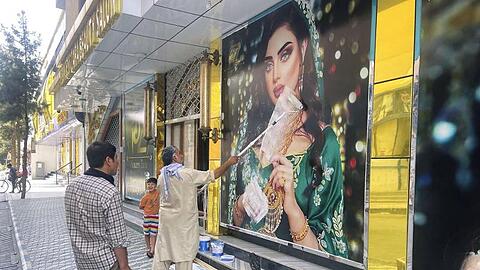 Ein Mitarbeiter eines Schönheitssalons übermalt am Sonntag in Kabul nach dem Einmarsch der Taliban ein großes Frauenpoträt.