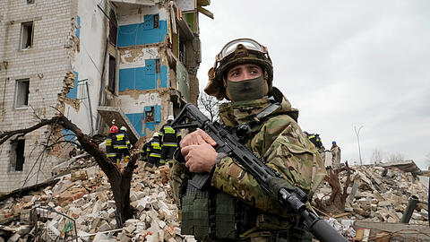 Borodjanka: Ein ukrainischer Soldat steht mit seinem Gewehr vor einem durch russischen Beschuss zerstörten Wohnhaus.