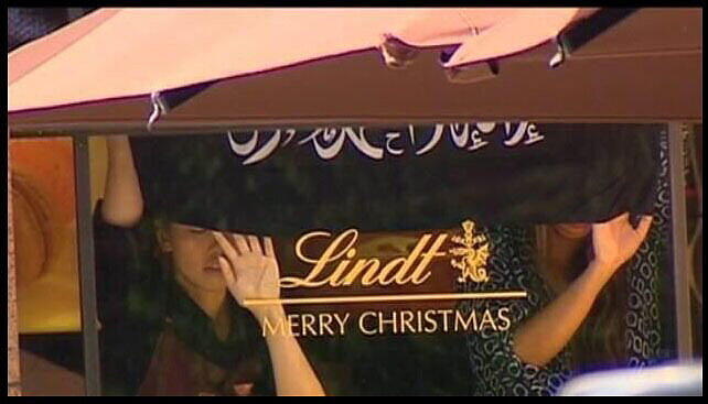 Zwei Geiseln müssen eine Islam-Fahne an die Scheibe des "Lindt"-Cafés halten.
