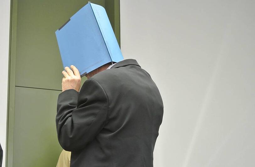 Hinter einem Aktendeckel verbirgt der Angeklagte sein Gesicht.
