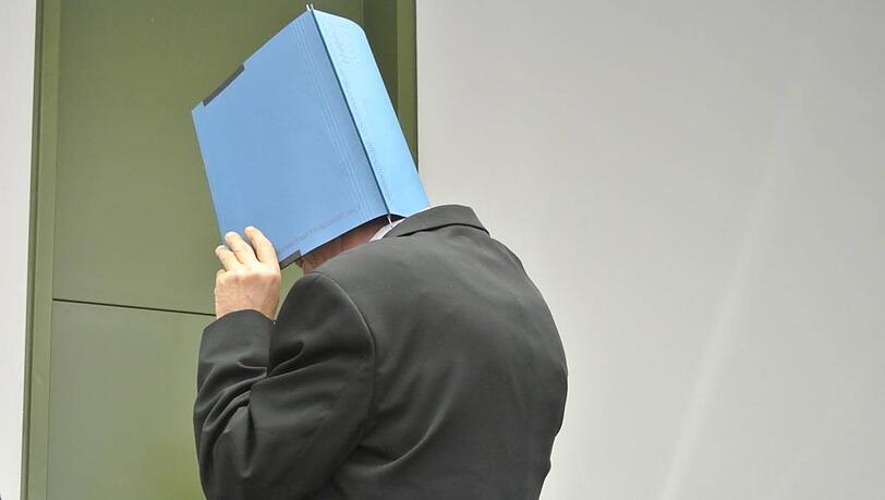 Hinter einem Aktendeckel verbirgt der Angeklagte sein Gesicht. Hinter einem Aktendeckel verbirgt der Angeklagte sein Gesicht.