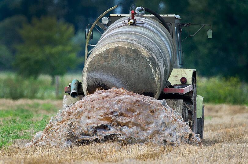 Ein Traktor mit Anhänger bringt auf einem Feld Gülle aus