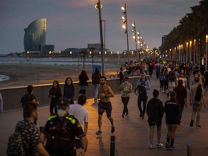 Menschen gehen bei Sonnenuntergang auf einer Strandpromenade spazieren und treiben Sport.