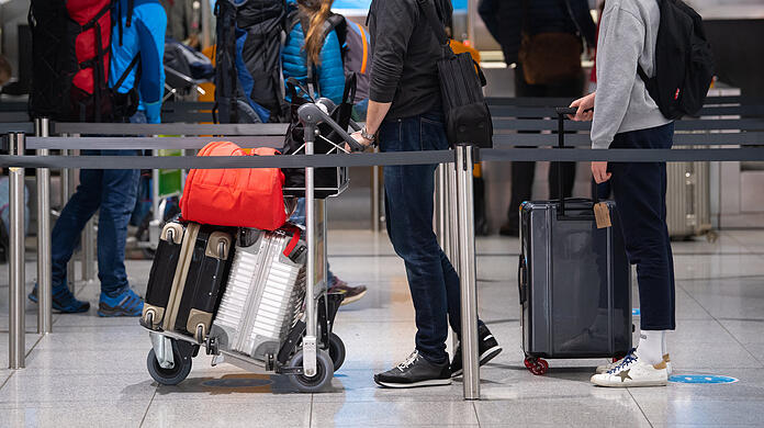 Reisende stehen am Flughafen München mit ihren Koffern am Check-In Schalter.