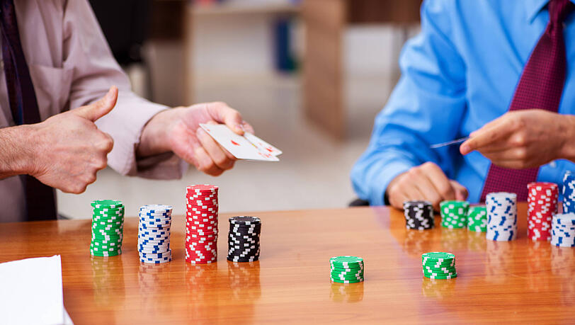Zwei Männer in Bürokleidung spielen Poker. Das Spiel kann helfen, bessere Entscheidungen zu treffen.