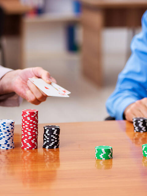Zwei Männer in Bürokleidung spielen Poker. Das Spiel kann helfen, bessere Entscheidungen zu treffen.