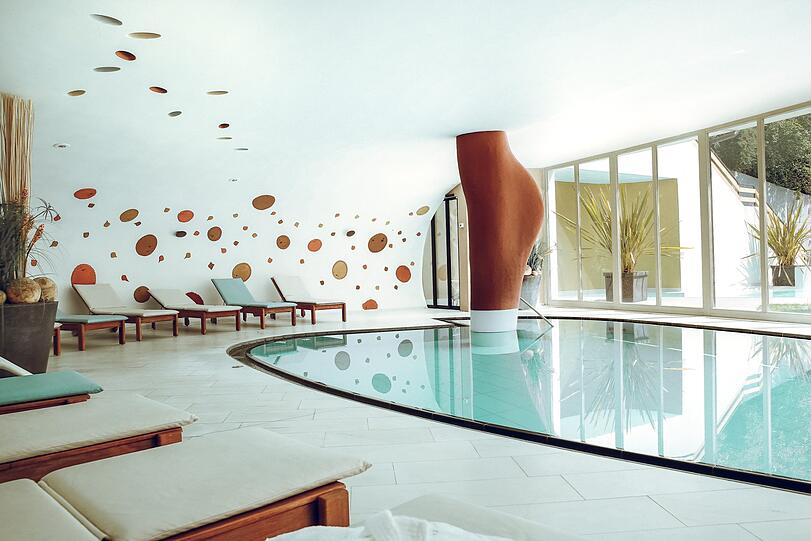 Er kommt mit einer ziemlich eigenwilligen Form daher, der indoor Pool im BOTANGO. Das schlichte Design des Schwimmbads hebt die Ausnahmeerscheinung hervor. Baden Sie von 7.00 bis 23 Uhr im 29°C warmen Wasser &ndash; und im Licht! Denn die gesamte Breite des Hallenbads ist raumhoch verglast und gibt den Blick auf Pool und Liegewiese draußen frei.
