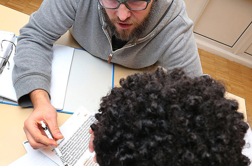 Ein Erzieher betreut in einem Gemeinschaftsraum der Familienhilfe in Würzburg einen 14-jährigen unbegleiteten Flüchtlingsjungen aus Eritrea bei dessen Deutsch-Hausaufgaben (Archivbild)