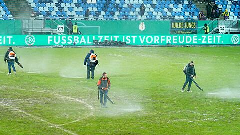 Arbeiter versuchten, Wasserlachen vom Spielfeld im Ludwigsparkstadion zu entfernen.
