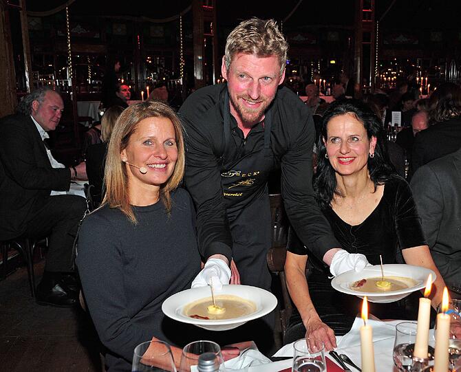 Der Schauspieler Martin Gruber serviert der Moderatorin Katrin Müller-Hohenstein (l) und Gabriele Kröner, Geschäftsführender Vorstand der Jose Carreras Leukämie Stiftung, beim Jose Carreras Charity Dinner im Schuhbecks teatro