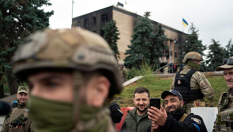 Der ukrainische Präsident Wolodymyr Selenskyj (M) macht in Isjum ein Selfie mit einem Polizisten.