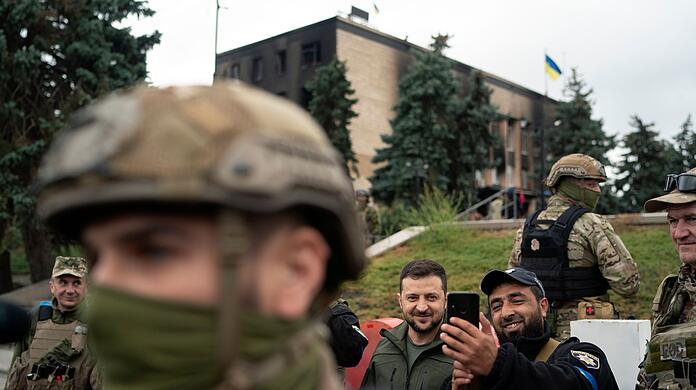 Der ukrainische Präsident Wolodymyr Selenskyj (M) macht in Isjum ein Selfie mit einem Polizisten.