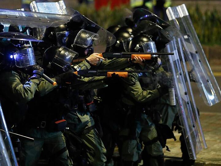 Polizisten richten Waffen auf Demonstranten.