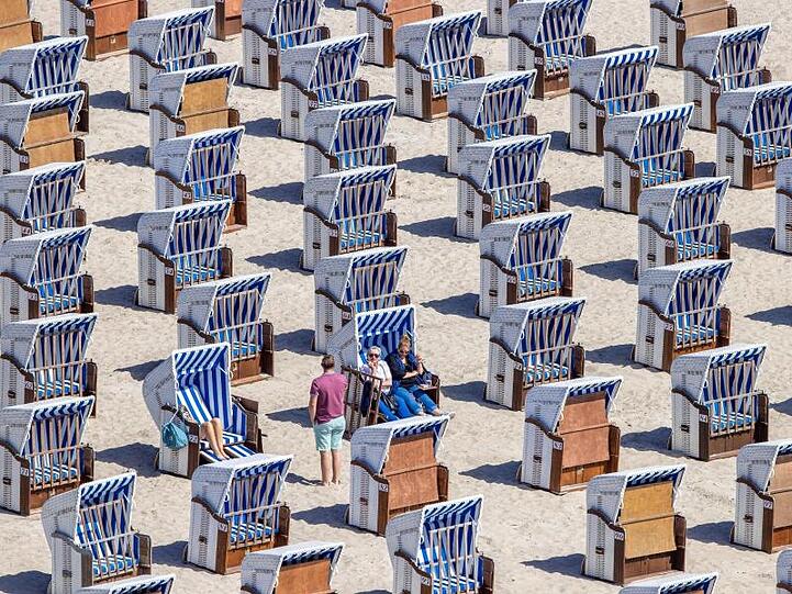 Erste Urlauber sitzen in Strandkörben am Ostseestrand in Warnemünde.